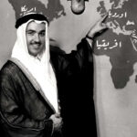 فهمي بصرامي يرتدي الزي السعودي والبشت ويشير إلى خريطة العالم خلفه يشرحها